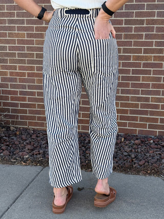 Person wearing black and white striped pants standing against a brick wall.