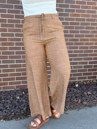 Person wearing brown plaid pants standing against a brick wall.