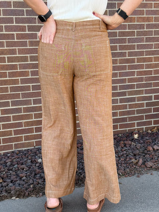 Person wearing brown plaid pants standing against a brick wall.