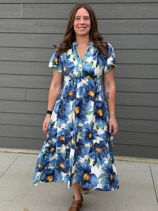 Woman wearing a blue floral dress standing against a gray wall.