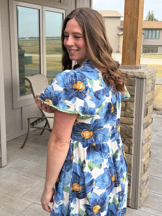 Woman wearing a blue floral dress standing on a porch.