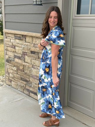 Woman wearing a floral dress standing outside a house.