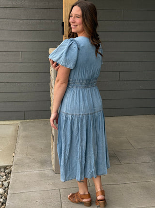 Woman wearing a blue dress standing against a gray wall.