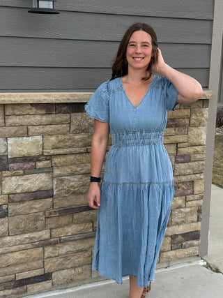 Woman in a blue dress standing against a stone wall.