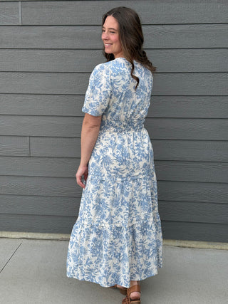 Woman wearing a blue floral dress standing against a gray wall.