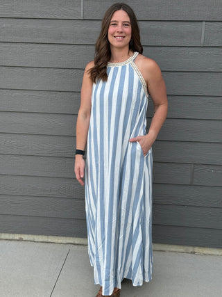 Woman wearing a blue and white striped dress standing against a gray wall.