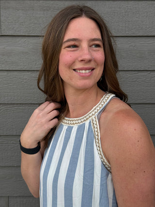Woman wearing a blue and white striped dress with decorative trim against a gray wall.