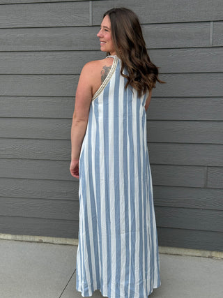 Woman wearing a blue and white striped dress against a gray wall.