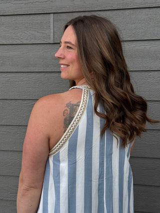 Woman wearing a blue and white striped dress with a decorative back, standing against a gray wooden wall.