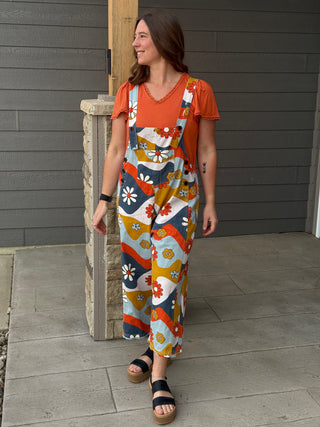 Woman wearing a colorful patterned jumpsuit standing against a gray wall.