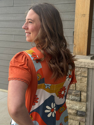 Woman wearing a colorful floral dress with an orange top, standing outdoors.