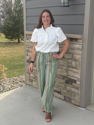 Woman wearing a white blouse and striped pants standing in front of a stone wall.