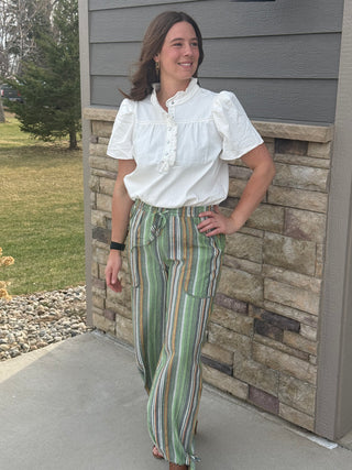 Woman in a white blouse and striped pants standing against a stone wall.