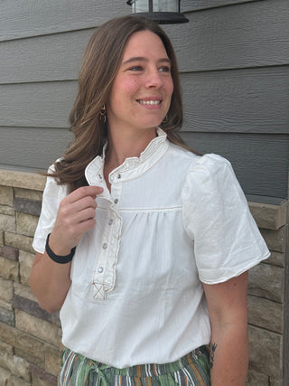 Woman wearing a white blouse standing against a gray siding wall.