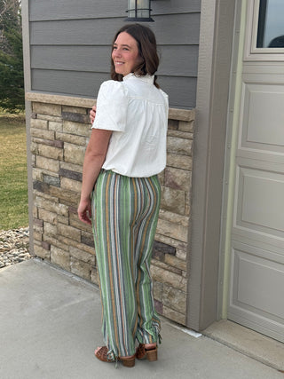 Woman standing outside a house wearing a white blouse and striped pants.
