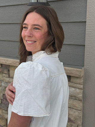Woman in a white shirt standing against a gray siding wall.
