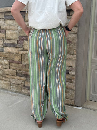 Person wearing a white shirt and colorful striped pants standing against a stone wall.