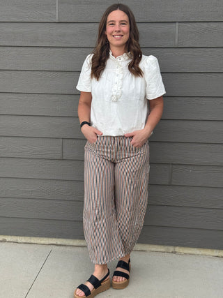 Woman wearing a white blouse and striped pants standing against a gray wall.