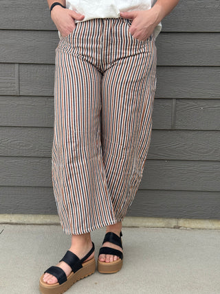 Person wearing striped pants and black sandals against a gray wooden wall.