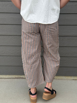 Person wearing a white top and striped pants standing against a gray wall.