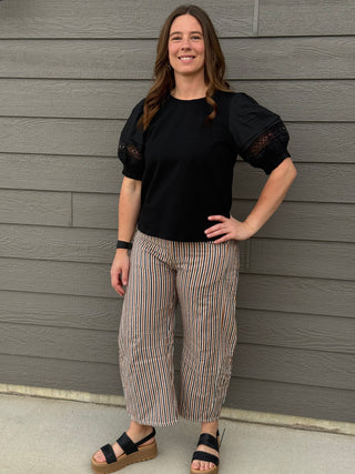 Woman wearing a black top and striped pants standing against a gray wall.