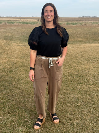 Woman standing in a field wearing a black top and brown pants.