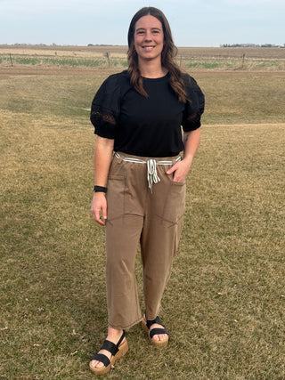Woman standing in a field wearing a black top and brown pants.