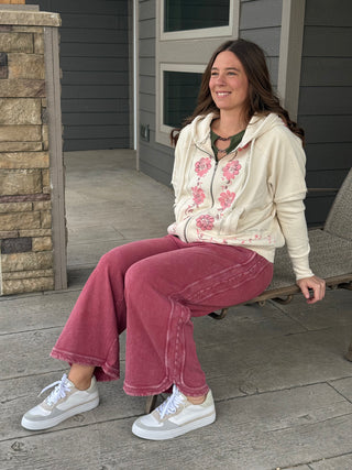 Woman sitting on a porch wearing a floral hoodie and pink pants.