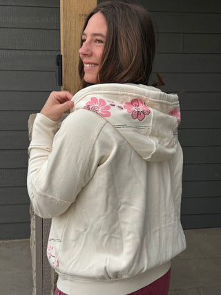 Woman wearing a white quilted jacket with floral designs against a dark wooden door.