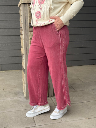Person wearing pink corduroy pants and a cream jacket with floral patterns, standing on a wooden deck.