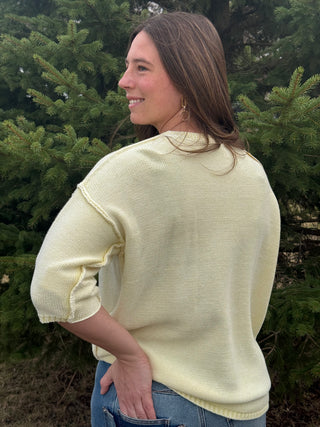 Woman wearing a light yellow sweater standing in front of green trees