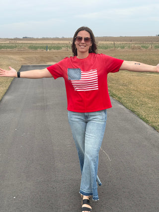 Person wearing a red t-shirt with an American flag design on a paved road.