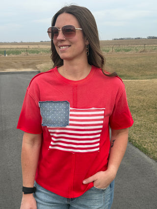 Woman wearing a red t-shirt with an American flag design outdoors.