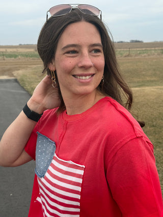 Woman wearing a red shirt with an American flag design, standing outdoors.
