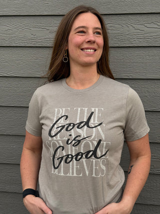 Woman wearing a gray t-shirt with text standing against a wooden wall.
