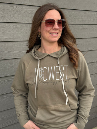 Woman wearing a green hoodie with 'Midwest' text, standing against a gray wooden wall.