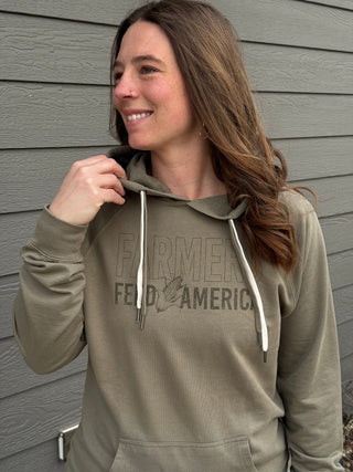 Woman wearing a green hoodie with text, standing against a gray wall.