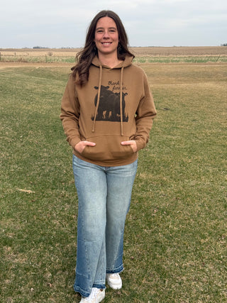 Woman wearing a brown hoodie with a graphic design, standing in an open field.