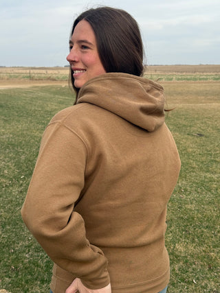 Woman wearing a brown hoodie standing in an open field
