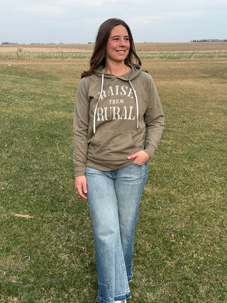 Woman wearing a hoodie with 'Raise the Rural' text in an open field.