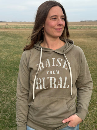 Woman wearing a hoodie with 'Raise Them Rural' text in a field