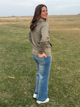 Woman standing in a field wearing a green jacket and blue jeans.