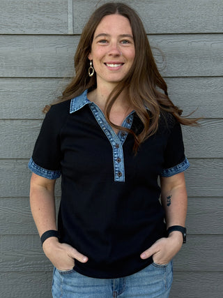 Woman wearing a black shirt with denim collar and cuffs against a gray wooden wall.