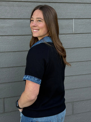 Woman wearing a black shirt with denim collar and cuffs against a gray wall