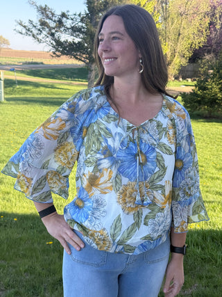 Woman wearing a floral blouse with blue, yellow, and green colors outdoors.