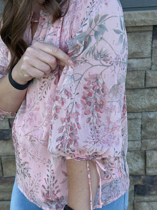 Person wearing a pink floral blouse against a stone wall background