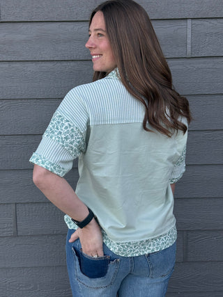 Woman wearing a light green blouse with floral lace details on a gray wall background