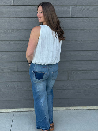 Woman wearing a white blouse and blue jeans standing against a gray wall.