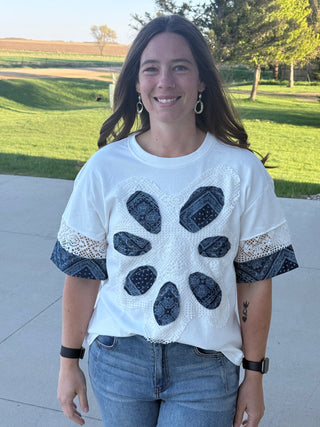 Woman wearing a white lace top with black abstract patterns outdoors.
