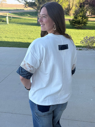 Woman wearing a white shirt with lace sleeves and a black patch on the back, standing outdoors.